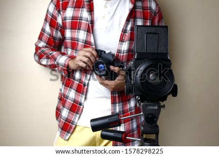 Photo of a man holding a 35mm film camera and standing behind a medium format film camera on a tripod