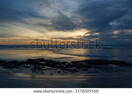 A Cloudy sunset on an empty beach in California with light reflecting off the water on a sandy beach with a rock formation from the waves