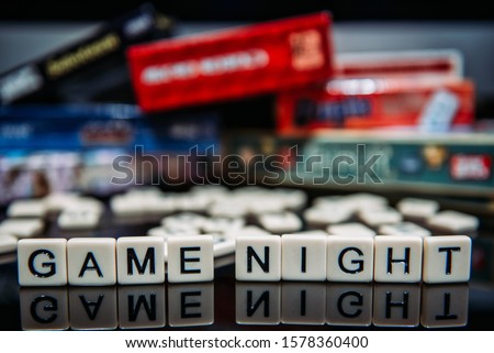 Game Night spelled out in letter tiles on black background with boardgames in the background