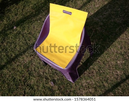 yellow Non Woven Bag isolate lying on plastic kids chair Green grass Background 