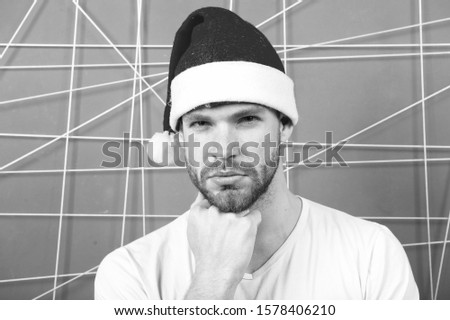 Macho in santa hat touch beard on serious face on pink background. Barbershop, grooming, male beauty. Christmas, new year, winter, holidays, celebration, party concept