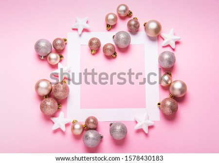 Christmas balls and white paper  frame on stylish pink table top view. Fashion background. Flat lay. Party mockup or invitation.