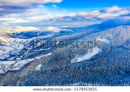 Snowy forest covers mountains on bright day, aerial landscape. Travelling on holidays concept