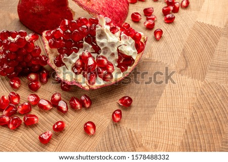 Cut ripe pomegranate fruit and pomegranate seeds on natural wooden background.
