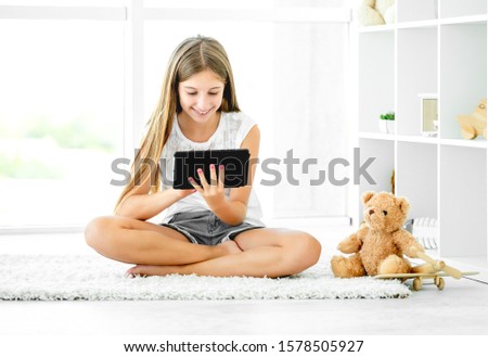 Happy girl using tablet computer sitting in playing room