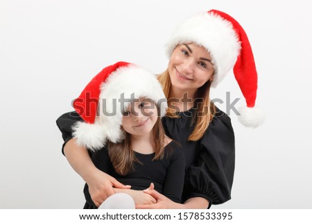 Mom in a santa hat hugs daughter on a white background in the studio. Concept for articles on family traditions and holidays of the New Year and Christmas.