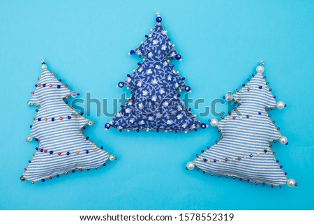 3 Handmade striped and floral textile fabric naive retro style Christmas tree ornament decorated with beads on blue background