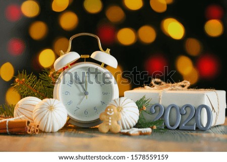 Alarm clock with Christmas decor and gift on table against defocused lights