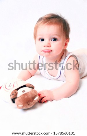 A small child lies on the floor with a toy on a white background. Photography of babies, children's emotions. Use in children's stores, websites, boards, etc.