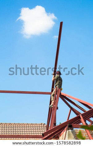 Welders Using iron oxide roofing frame That is being built on a high ground, outdoor.