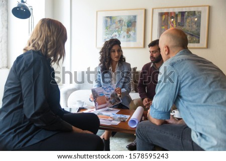 Architect showing building picture to customers. Group of people sitting in living room at home and talking. Architect or professional communication concept