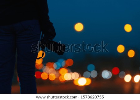 Young holding the camera with abstract blurred light in night time of urban with bokeh background.