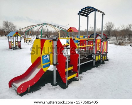 The photo shows a children's playground, where there is a swing and much more in winter