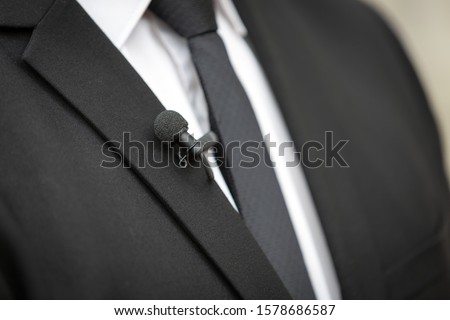 Close up picture of a  clip on microphone on a black suit