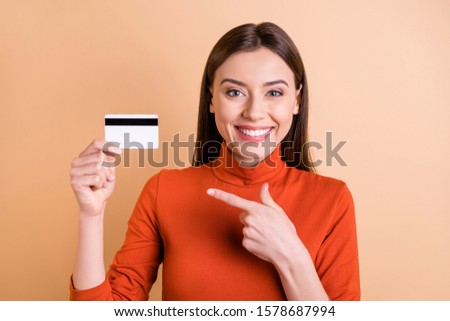 Photo of charming cute cheerful girlfriend showing you that using electronic way of payment is more comfortable holding credit card with her hand pointing isolated beige pastel color background