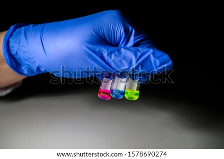 Scientist holding three colourful solution in different LCMS glass vial on a white bench with black background for medical research in a chemistry laboratory. Corona Virus and vaccine development. 
