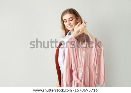 Female worker of modern dry-cleaner with clothes on light background
