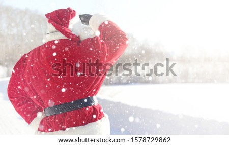 Santa Claus comes with gifts from the outside. Santa in a red suit with a beard and wearing glasses is walking along the road to Christmas. Father Christmas brings gifts to children.