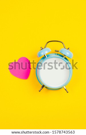 Vintage blue blank alarm clock on a yellow background with pink sticker