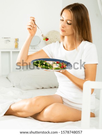 Young beautiful woman eating vegetable salad in her bed