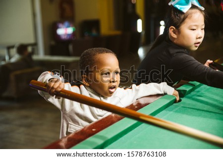 An Asian girl and a boy from Africa playing snooker. Children and sports