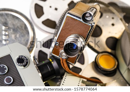 Vintage movie cameras lie on the background of reels with film strip. For your design.