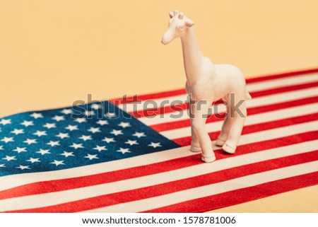 White toy giraffe on american flag on yellow background, animal welfare concept