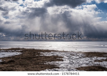 the high-contrast picture of streams of light breaking through snow clouds on the shore of the frozen Gulf of Finland creates a dramatic mood and evokes a response from the viewer