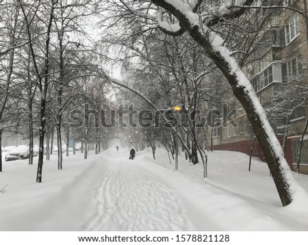 Heavy snowfall in the city. All around in the snow, away along the house on the snowy road is a man with a bag. Photos from a mobile phone in Moscow 2018. 