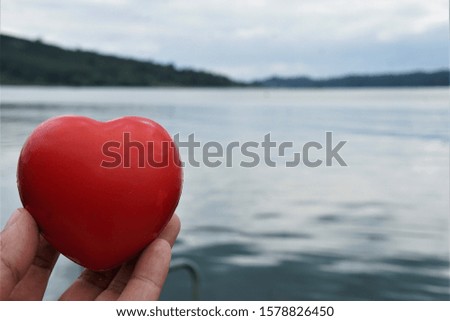 Selective the focus on the heart shaped rubber ball in hand that is projected into the air, with a blurred background of the water surface. The mountains and the twilight sky.