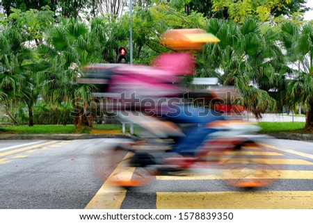 A motorcycle becomes a motion blur as the driver speeds across a yellow pedestrian crossing in haste. Fast motion streaks of a bike and rider as it dashes rapidly past over a crosswalk. Royalty-Free Stock Photo #1578839350