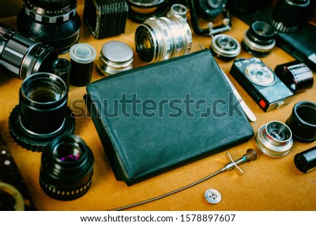 Retro mockup, retro black pack for photo paper in center and vintage photographic accessories and quipments around on Wooden Background.
