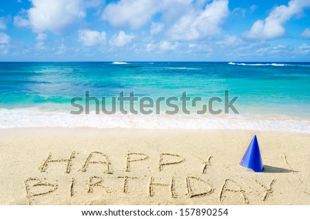 Sign "Happy Birthday" with hat on the sandy beach by the ocean