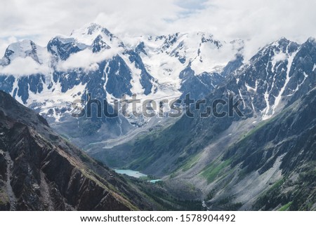Atmospheric alpine landscape with massive hanging glacier on giant rocks and valley with mountain lakes. Big glacier tongue. Low clouds over snowbound mountains. Majestic scenery on high altitude.