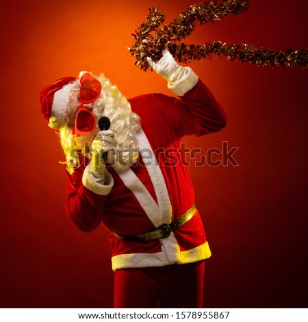 Santa Claus in large pink glasses and with a red garland of tinsel in his hands dancing and posing on a dark red background