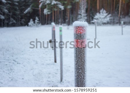 car parking lot enclosing poles at Kemeri bog trail. Snowy and frozen pillar after snowfall. Ice textured post with red reflective markings. Traveling and driving by car in winter season.