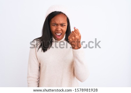 Beautiful young african american woman wearing turtleneck sweater and winter hat angry and mad raising fist frustrated and furious while shouting with anger. Rage and aggressive concept.