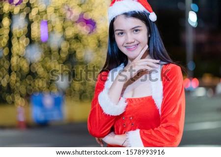 Portrait of a cheerful Asian woman wears Santa Claus costume presents gift for the Christmas festival and new year celebration with beautiful bokeh light background.