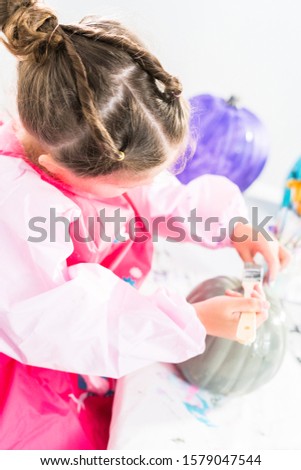 Little girl painting small craft pumpkin with gray acrylic paint.