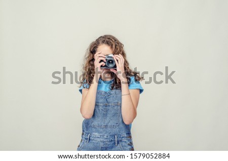 Curly brunette girl in denim overalls is holding a vintage film camera in her hands. Takes a picture