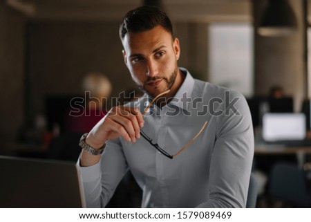 Close up of a bearded businessman wearing glasses and sitting at his laptop and typing.