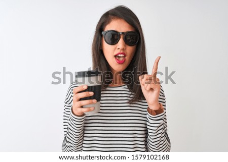 Chinese woman wearing sunglasses drinking take away coffee over isolated white background surprised with an idea or question pointing finger with happy face, number one