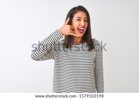 Young beautiful chinese woman wearing striped t-shirt standing over isolated white background smiling doing phone gesture with hand and fingers like talking on the telephone. Communicating concepts.