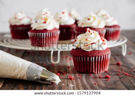 Red velvet cupcakes on a cooling rack and a pipping bag on a rustic wooden table Royalty-Free Stock Photo #1579137904