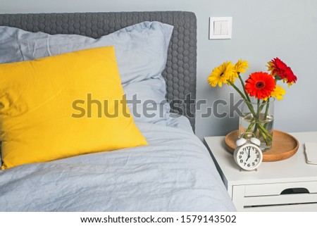 Modern bedroom interior with bright decorative pillow on the bed and brigh flowers on the nightstand.