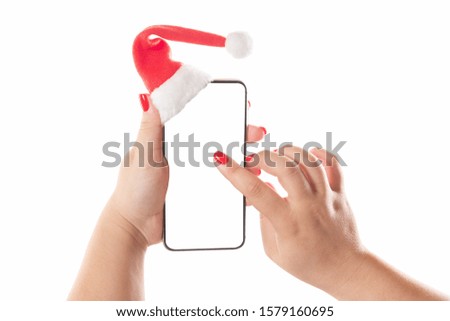 Female hands holding mobile smart phone with santa hat isolated on white background. Blank white screen. Concept of Christmas congratulation