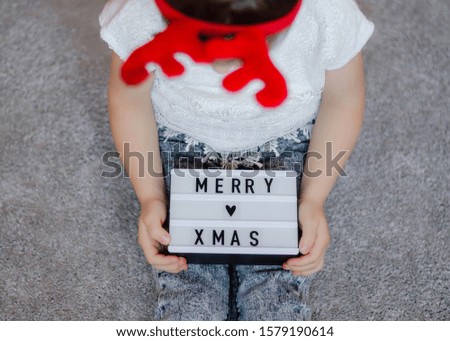 Kid Girl holds lightbox on which is written Merry Christmas. close-up. christmas card