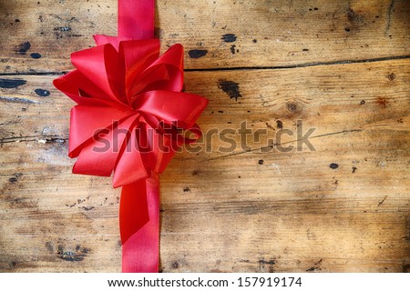 Decorative red ribbon and bow on a rustic wood background with copyspace to celebrate a Merry Christmas, romantic Valentines Day or birthday with a greeting card