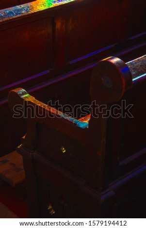 Old church wooden benches colored with sunlight filtered through the stained glass window. Selective focus on pew armrest. God mercy, miracle, hope, religion concepts. Spiritual mystery background.