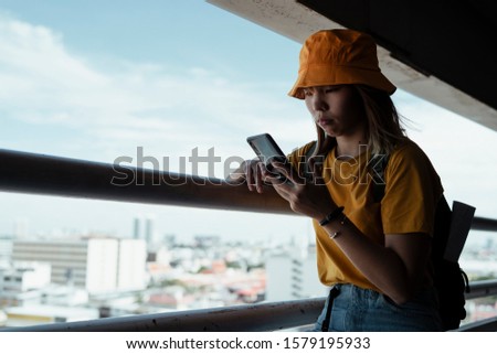 Backpacker girl standing at the handrail watching the photo in her smartphone.